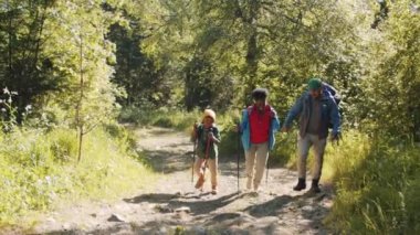 Afro-Amerikan anne, Kafkas baba ve küçük melez oğlunun yaz tatilinde doğa yürüyüşü yaparken yürüyüş direkleri ve sırt çantalarıyla yürümelerini gösteren bir fotoğraf.