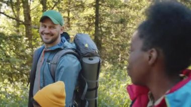 Beyaz bir baba, siyah bir anne ve melez bir oğulun ormanda yürüyüş direkleri ve sırt çantalarıyla yürürken, güneşli bir yaz günü yürüyüş yaparken gülümserken ve konuşurken çekilmiş el kamerası görüntüleri.