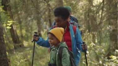 Genç Afro-Amerikalı bir kadın yürüyüş direkleri ile yürüyor ve ormanda yürüyüş yaparken küçük melez bir oğul ve beyaz bir kocayla konuşuyor.