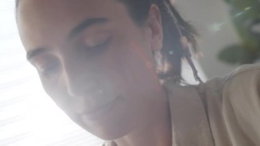 Hollanda açısı, genç beyaz kadının evde makrome süsleme yaparken aşağı eğildiğini gösteriyor.