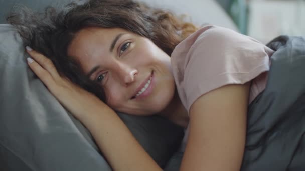 年轻美丽女人的画像 一头卷曲的黑发躺在床上 看着相机 面带微笑 — 图库视频影像