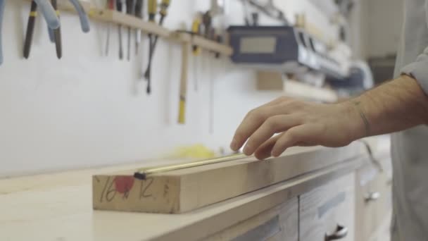 在他的橱柜作坊工作时 用胶带把白种人年轻熟练的木工的特写和面部照倾斜 在木板上放下 并画铅笔记号 — 图库视频影像