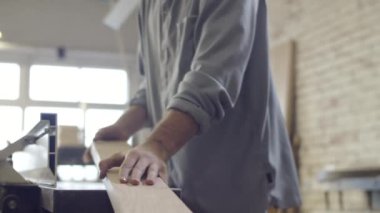 Güvenlik gözlükleri takan beyaz tenli genç marangozun yakın planda çekilmiş fotoğrafları. Katı ahşabı törpülüyor, sonra kaldırıyor, bir gözünü kıstırıyor ve kusurları kontrol ediyor.