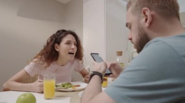 Beyaz adamın aile yemeği sırasında akıllı telefon kullandığını gösteren belden yukarı bir fotoğraf, histerik bir eş ona sitem ediyor, bağırıyor, telefonu kapıyor ve şok olmuş bir adamın suratına tokat atıyor.