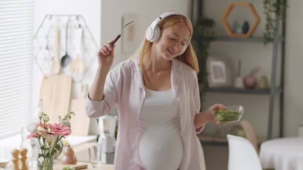 Telsiz Kulaklıklı Neşeli Hamile Kadın Elinde Salata Çatalla Evde Müzik — Stok video