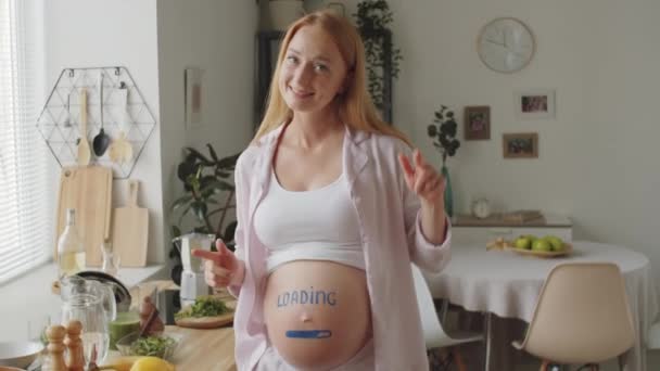 在厨房里 带着装载标志和进度条 在怀孕的孕妇肚皮舞上画着正中的孕妇照片 看着相机 面带微笑 — 图库视频影像