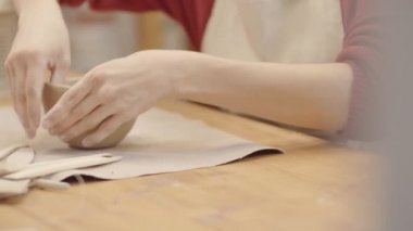 El sanatları atölyesinde kilden kase yontan genç, beyaz kadın çömlekçinin yakın çekim görüntüsü. Tek elle tutuyor ve dikkatlice yüzeyi parmaklarıyla düzleştiriyor.