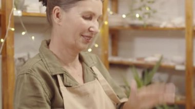 Önlüklü mutlu Kafkas bayanın el ve yüzlerinin yakın plan çekimleri. El sanatları atölyesindeki seramik atölyesinde çiğ çamur topunu şekillendiriyor ve dövüyordu.