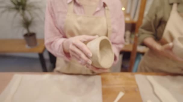 放大的特写镜头是穿着围裙和条纹衬衫的难以辨认的女陶工的手 他们在陶瓷工作室里做陶瓷碗 并轻轻抚摸着手指抚平表面 — 图库视频影像