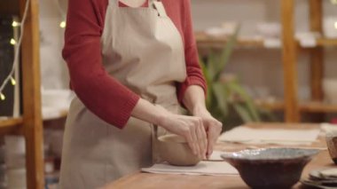 Beyaz tenli, kızıl saçlı, kazaklı, önlüklü, seramik atölyesinde toprak kabı yontan genç bir kadının belden yukarı portresi çekimleri. Sonra da mutlu bir gülümsemeyle kameraya bakıyor.