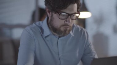 Karanlık ofisindeki masasında oturan ve dizüstü bilgisayarda çalışan yorgun sakallı adamı yukarı kaldır, sonra gözlüklerini çıkar ve gözlerini ovuştur.