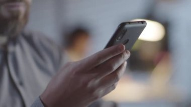 Karanlık ofisteki lambalarla aydınlatılmış cep telefonunda yazan tanınmayan sakallı adamı yakından çek.