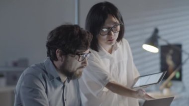 Tabletli ve sakallı bir adamla Asyalı neşeli iş kadınının yavaş yavaş takibi ve dizüstü bilgisayarlı adam akşam karanlık ofiste üzerinde çalıştıkları projeyi tartışıyorlar.