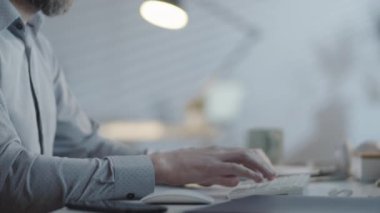 Karanlık ofisinde masasında oturan tanınmayan sakallı bir iş adamının yavaş elleriyle iz sürüp bilgisayar üzerinde çalışıyor.