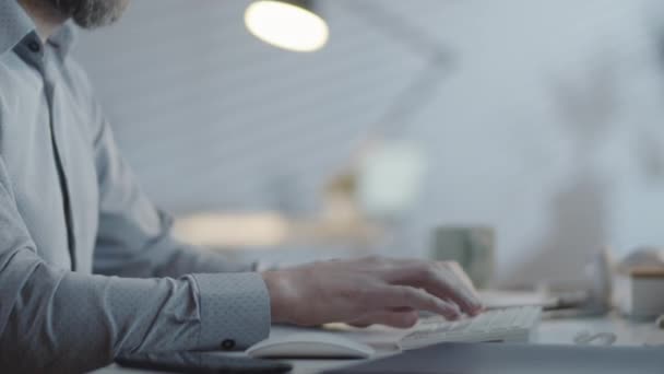 暗いオフィスで彼の机に座って コンピュータ上で作業している認識できないひげそりのビジネスマンの手の遅い追跡 — ストック動画