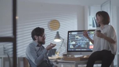 Asyalı mutlu iş kadını ve sakallı iş adamının fotoğrafının izini sürüyorum. Gözlüklü, pizza yiyen ve akşam vakti karanlık ofiste sohbet eden.