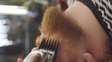 Beyaz adamın dikey yakın çekimi. Arkasına yaslanıp sakalını berbere kırptırıyor.