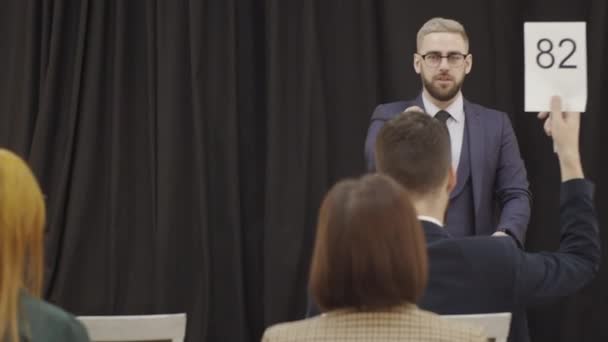 Elegante Leiloeiro Masculino Lectern Apontando Para Pás Anunciando Propostas Enquanto — Vídeo de Stock