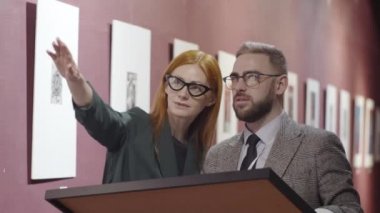 Galeri müdürü, erkek meslektaşına sergi salonunu hazırlarken sanat eserlerini nereye koyması gerektiğini söylüyor.