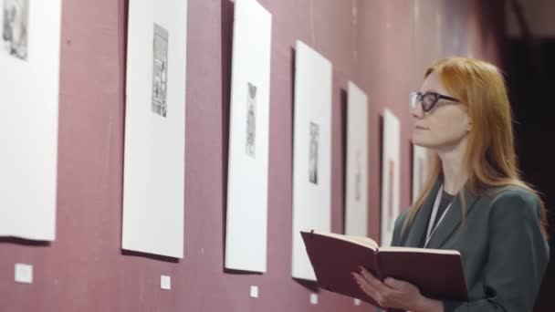 Intelligent Rödhårig Kvinna Glasögon Tittar Konstverk Galleriet Och Antecknar Anteckningsblock — Stockvideo