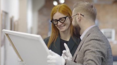 Beyaz eldivenler konusunda deneyimli bir erkek sanat uzmanı çerçeveli resim tutuyor ve bunu galeride birlikte çalışırken bayan meslektaşımla tartışıyor.