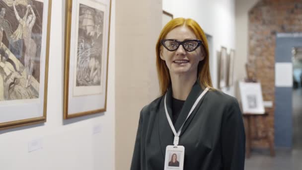 美术馆里 站在墙边 凝视着镜头 面带微笑的迷人红头发女人的画像 她脖子上挂着游客徽章 — 图库视频影像