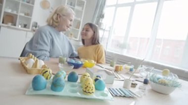 Mutfak masasında boyanmış Paskalya yumurtalarıyla otururken gülümseyen ve sarılan mutlu küçük kızı ve sevgi dolu büyükanneyi yakınlaştır.