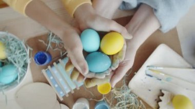 Üst manzara, ellerinde mavi ve sarı renklere boyanmış Paskalya yumurtaları tutan küçük kız ve büyükannenin görüntüsünü yakınlaştırıyor.