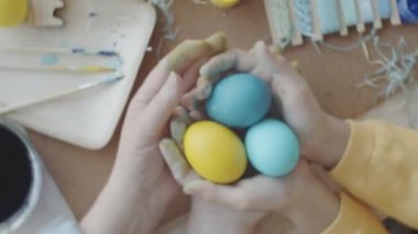 Üst manzara, el sanatları malzemeleriyle boyanmış Paskalya yumurtalarını tutan büyükanne ve küçük kızın ellerini yakınlaştırıyor.