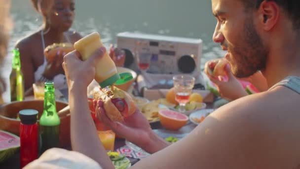 Młody Człowiek Dodając Musztardę Hot Doga Jedząc Siedząc Przy Stole — Wideo stockowe