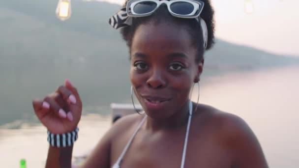 ワイングラスを持っている若い美しいアフリカ系アメリカ人女性の胸のショット カメラで笑顔と友人と湖のパーティーで踊る — ストック動画