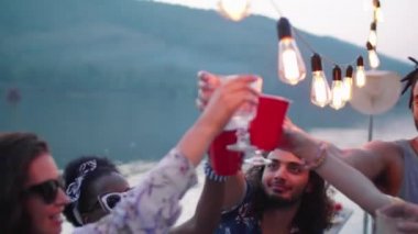 Çelenkle süslenmiş iskelede dans eden ve akşamları göl partisinde kadeh tokuşturarak içki içen çok ırklı genç kadın ve erkeklerden oluşan neşeli bir grup.