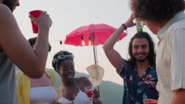 Orta Doğulu neşeli adamın kafasında bira şişesiyle dans ettiği, gülümsediği ve göl partisinde eğlenirken arkadaşlarıyla kadeh kaldırdığı düşük açılı çekim.