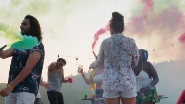 夏の湖パーティーで色の煙爆弾で踊る若い幸せな多民族の友人の低角度ショット — ストック動画