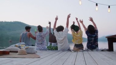 Arka plan, genç çoklu etnik arkadaşların tahta iskelede otururken ve kollarıyla dans ederken görüntüsünü yakınlaştırır.