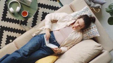 Evdeki kanepede uzanmış kitap okuyan genç melez kadının manzarası