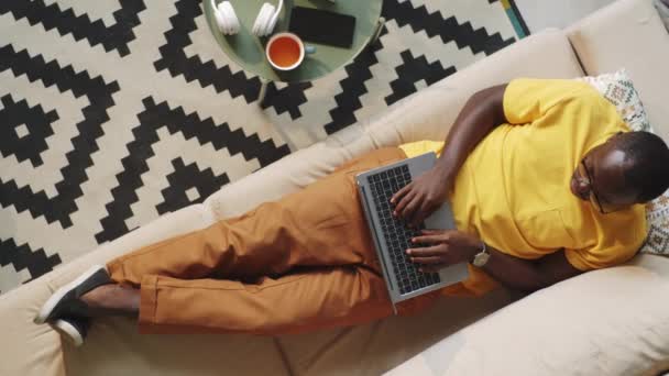 Надновий Постріл Афро Американського Чоловіка Лежить Дивані Друкує Ноутбуці Працюючи — стокове відео