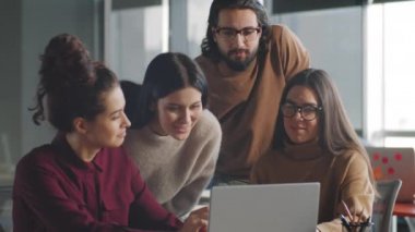 Genç ortadoğulu iş adamı ve üç bayan meslektaşı, ofiste çalışırken dizüstü bilgisayarda proje tartışıyor ve gülümsüyor.