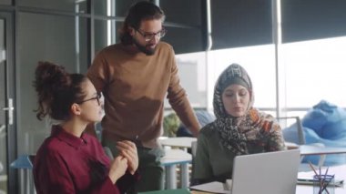 Orta Doğulu iş adamı, ofiste birlikte çalışırken çeşitli kadın meslektaşlarıyla dizüstü bilgisayarla proje tartışıyor.