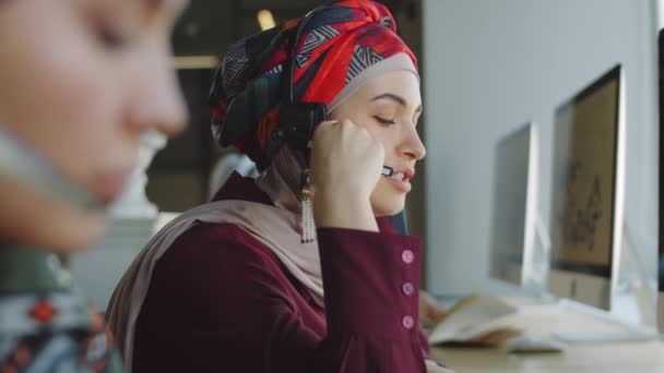 Webコールで話すヘッドセットでイスラム教徒の女性マネージャー コールセンターで作業しながらノートを取り コンピュータを使用して — ストック動画