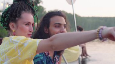 Kafkasyalı genç bir kadın saçlarını dikmiş gülümsüyor ve neşeli bir Orta Doğulu adamla konuşuyor. İskelede birlikte oturuyor ve göl manzarasının tadını çıkarıyor.