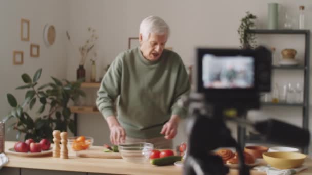 新鮮な野菜を実証し 家庭で料理のVlogを記録しながら カメラで話す高齢者のラックフォーカスショット — ストック動画