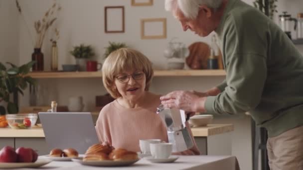 Positive Elderly Woman Sitting Kitchen Table Laptop Chatting Husband Pouring — Stock Video