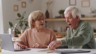 Üst düzey çift masada oturuyor, dizüstü bilgisayar kullanıyor, finansal evrakları inceliyor ve aile bütçesini evde tartışıyor.