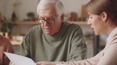 Evrakları inceleyen yaşlı bir çift, kadın finans danışmanıyla yapılan yatırımlar hakkında tartışıyorlar.