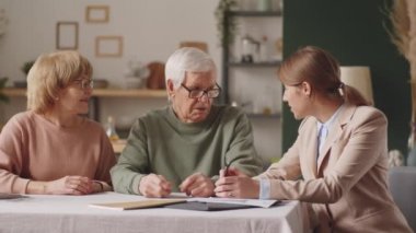 Yaşlı çift ve kadın mali danışman tartışıyorlar, sonra birlikte kameraya bakıp evde otururken gülümsüyorlar.