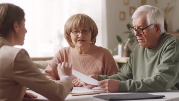 高齢者や女性がテーブルに座って契約書を読み 自宅で相談する際に女性保険代理店と詳細を話し合う — ストック動画