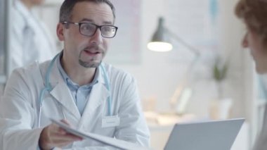 Ensesinde steteskop olan profesyonel erkek doktor kadın hastayla konuşuyor ve klinikte muayene sırasında imzalaması için ona tıbbi hizmet veriyor.