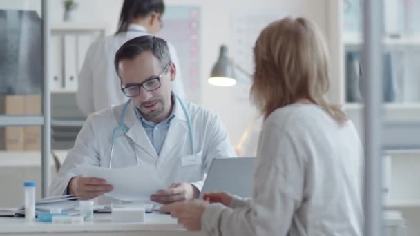 Profesionální Mužský Lékař Laboratorním Plášti Brýlích Čtení Lékařské Anamnézy Pacientky — Stock video