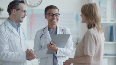 Neşeli, melez kadın doktor ve beyaz erkek meslektaşının belden yukarısını çek ve muayenehanedeki sarışın kadınla gülümse ve konuş.
